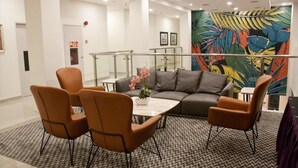 A modern living room with a gray sofa, orange chairs, a white coffee table, and a patterned rug.