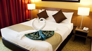 A hotel room with a neatly made bed, two bedside lamps, a telephone on the nightstand, and a red curtain.