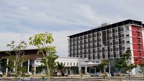 A modern hotel with a multi-story structure, a covered entrance, and a parking area with several cars.