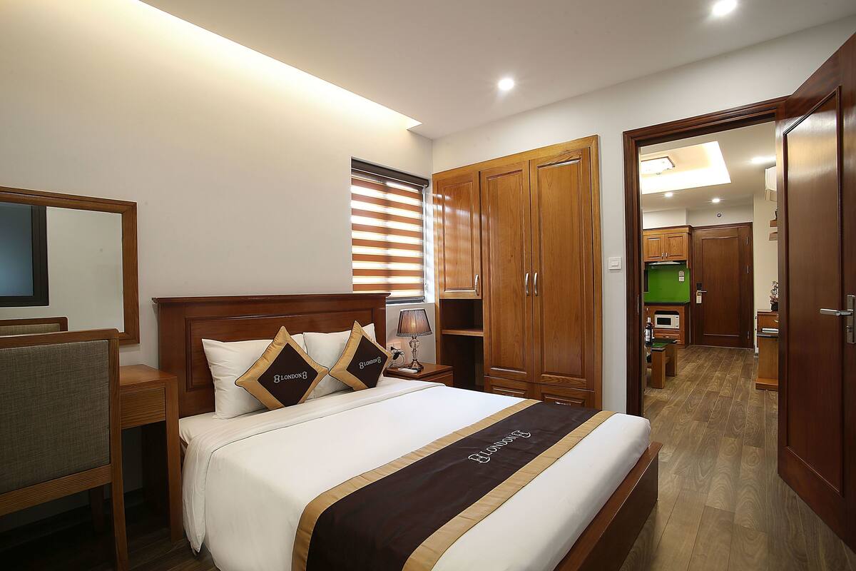 A hotel room with a bed, wooden wardrobe, a desk, and a mirror.