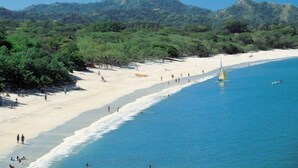 A beach with a clear blue sea, sandy shore, and a sailboat. - Luxury Oceanview Penthouse -
Private Beach Club Access -
Reserva Conchal (Brasilito)