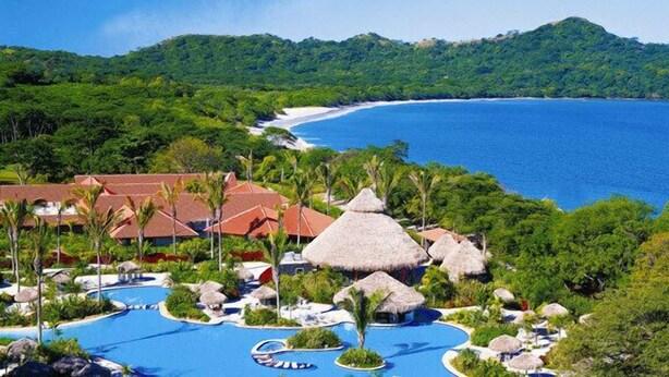 A resort with a large swimming pool, thatched-roof structures, and lush greenery. - Luxury Oceanview Penthouse -
Private Beach Club Access -
Reserva Conchal (Brasilito)