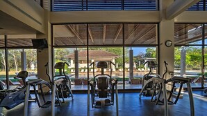 A gym with cardio machines, large windows, and a view of a building outside. - Luxury Oceanview Penthouse -
Private Beach Club Access -
Reserva Conchal (Brasilito)