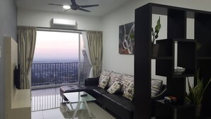 Un salón moderno con un sofá negro, una mesa de centro de vidrio y vistas de la ciudad a través de grandes ventanales.