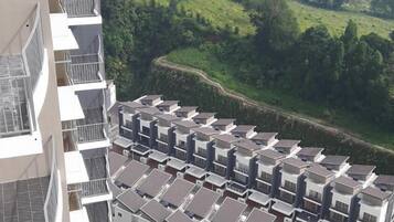 A high-rise residential building with multiple balconies, a swimming pool, and a view of a green landscape with distant hills.
