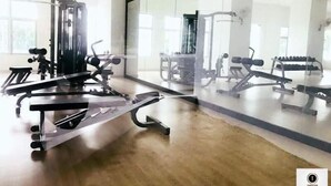 Un gimnasio con diferentes máquinas de ejercicio y pesas, ventanas amplias y un muro de cristal.