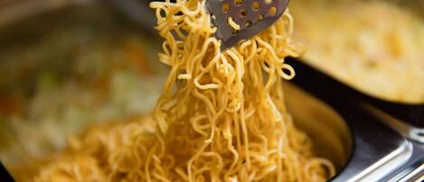 A close-up of a metal strainer lifting noodles from a container.