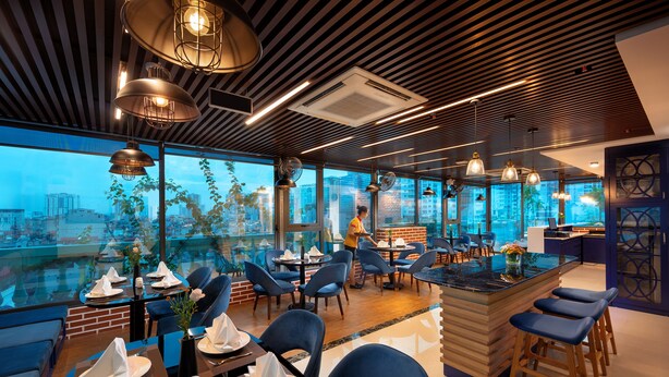 Een modern restaurant met een hoge plafond, grote ramen en een bar in het midden.
