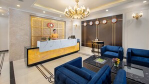 Een hotel lobby met een receptiebalie, blauwe banken, een kroonluchter en klokken aan de muur.