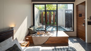 A modern bedroom with a large sliding glass door leading to a pool area, a cozy seating area with a blanket and books, and a wooden headboard. - Cherlock Hotel (Chiang Mai)