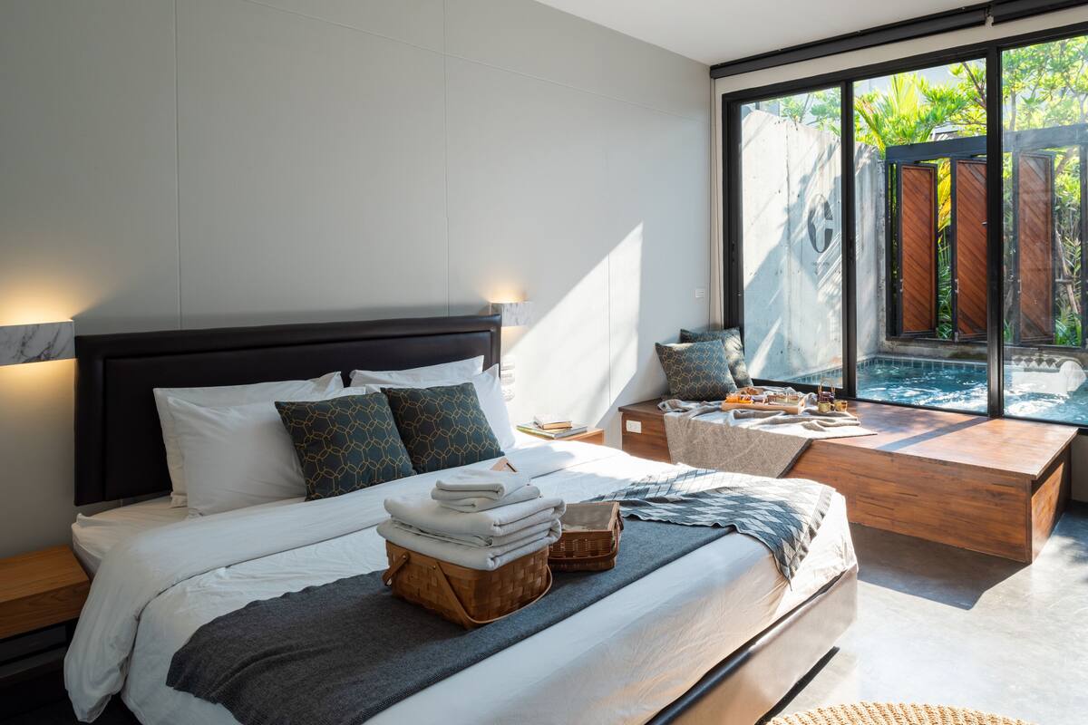 Un dormitorio moderno con una cama grande, mesitas de noche, un banco de madera y vistas al exterior.