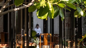 An outdoor seating area with wooden tables and chairs, surrounded by glass walls and greenery. - Cherlock Hotel (Chiang Mai)