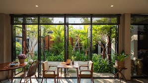 A sunlit room with a large window, a wooden table, and chairs. - Cherlock Hotel (Chiang Mai)