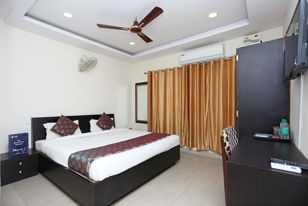 A modern hotel room with a large bed, a ceiling fan, a TV, and a desk with a remote control.