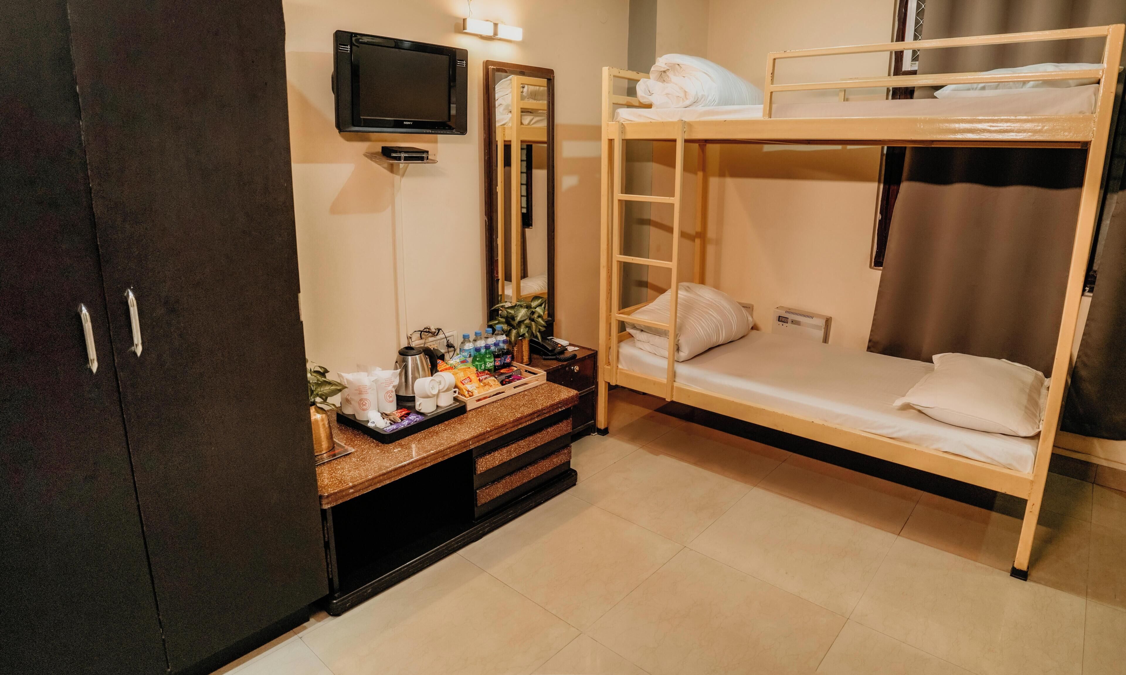 A bunk bed room with a TV, a mirror, a desk with toiletries, and a wardrobe.