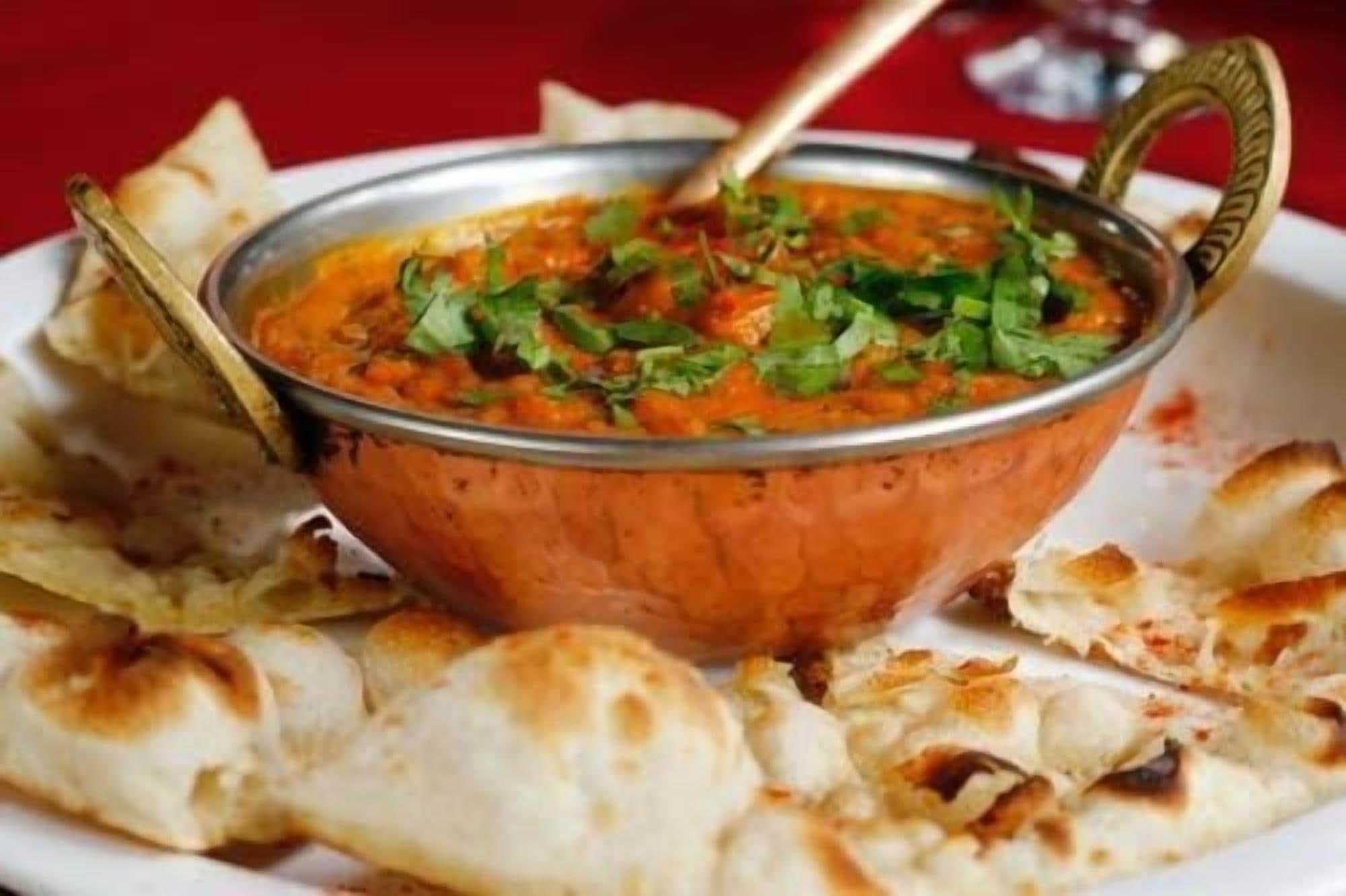 A bowl of curry with naan bread on a plate.