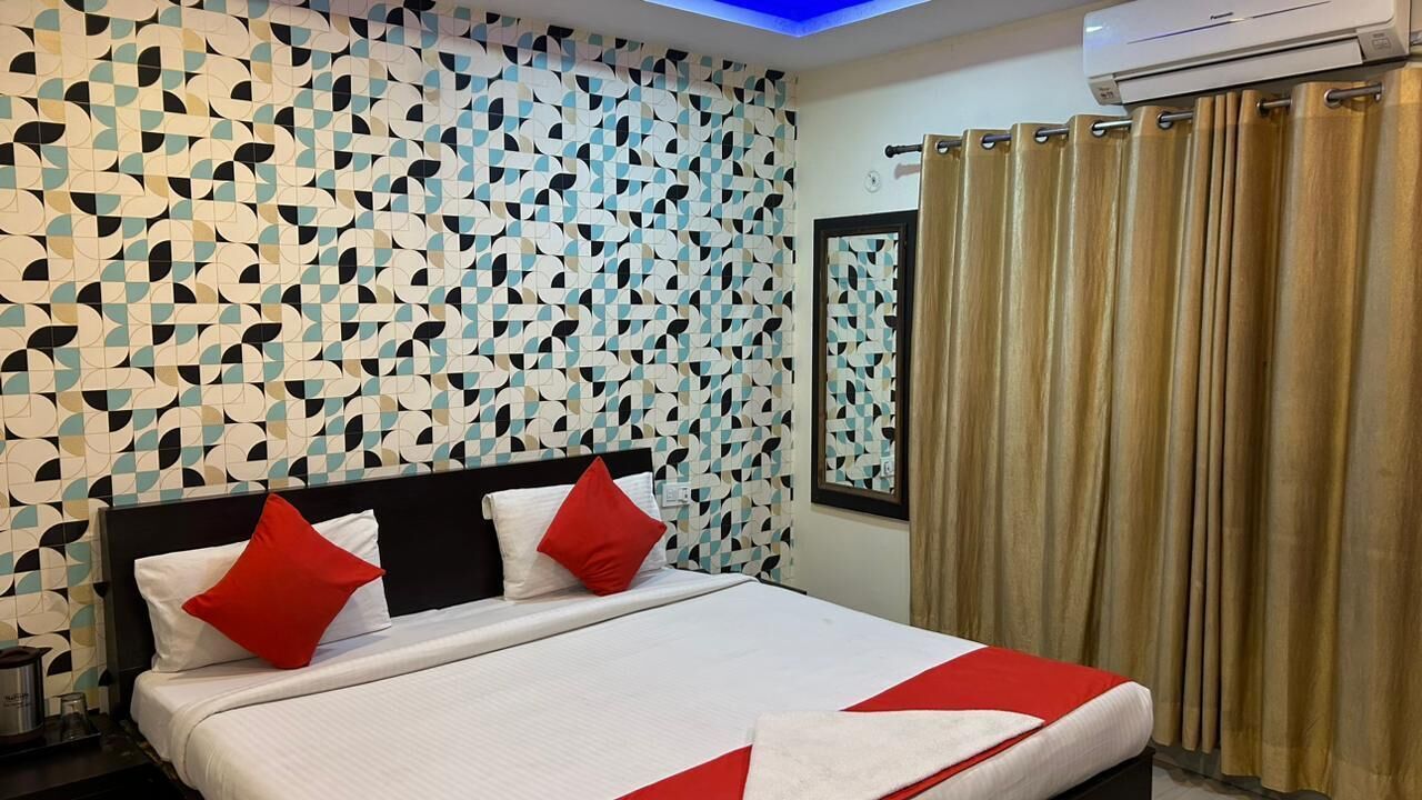 A hotel room with a geometric patterned wall, a bed with red and white bedding, and a curtain on the window.