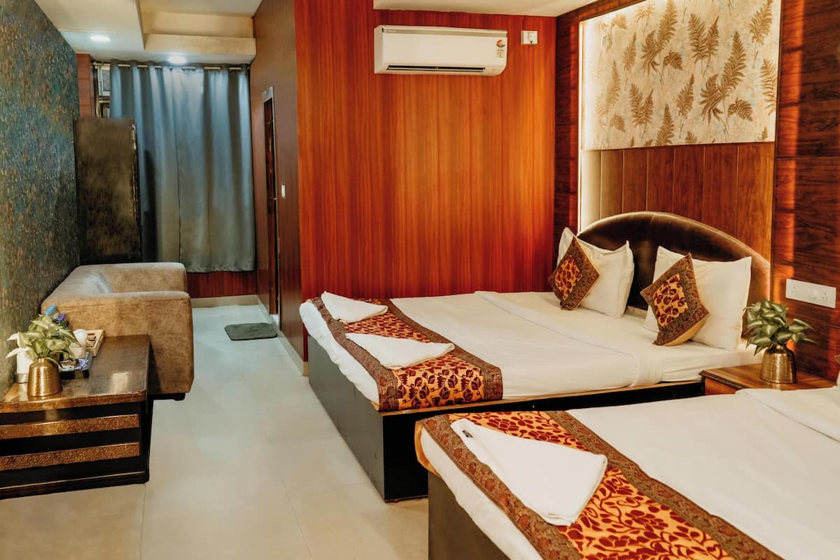 A hotel room with two beds, a sofa, a small table, an air conditioning unit, and a wall-mounted artwork.