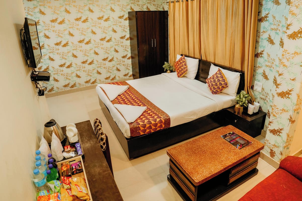 A hotel room with a bed, a TV, a desk with a computer, a red sofa, and a small table.