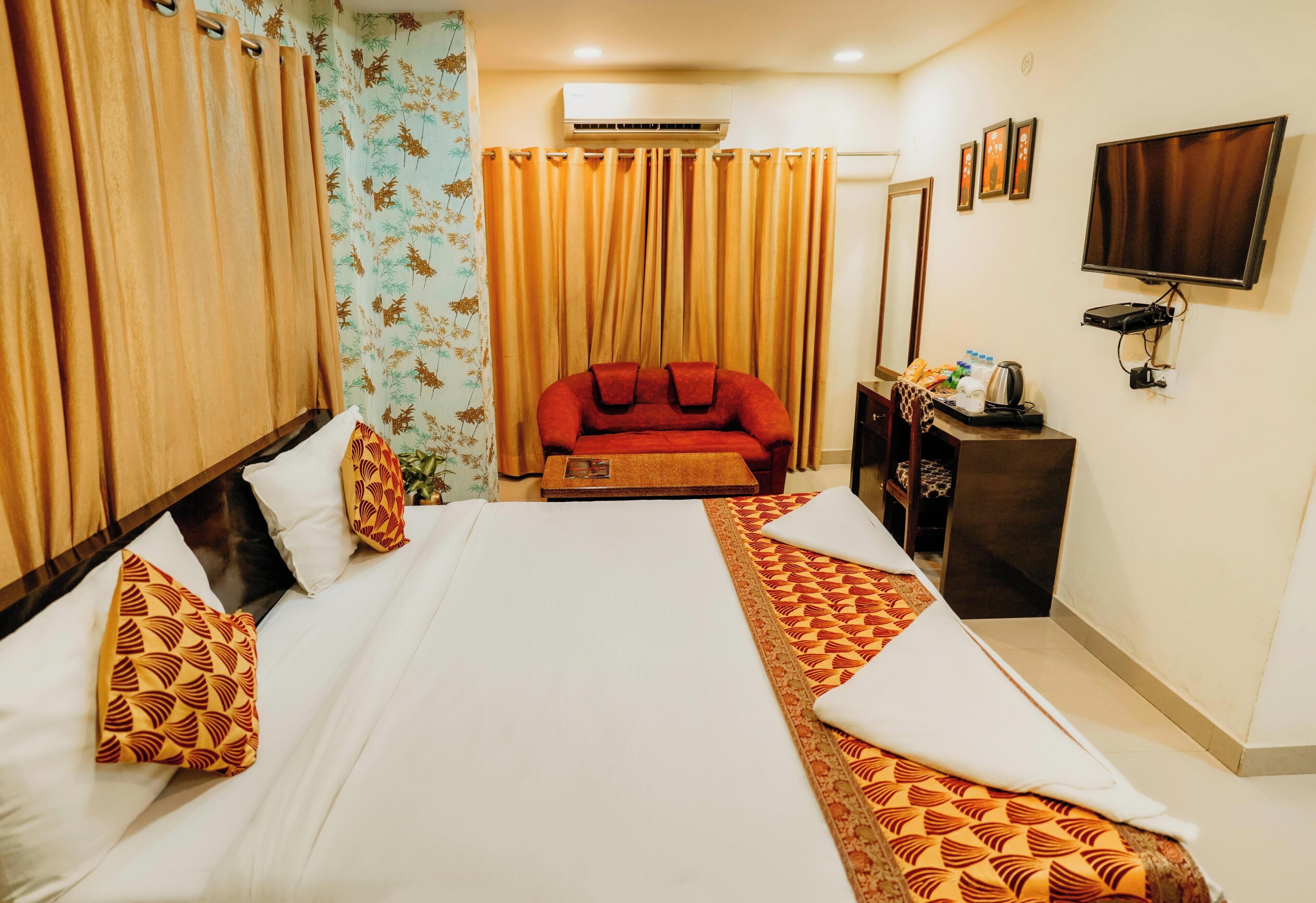 A hotel room with a bed, curtains, a sofa, a TV, and a desk with a mirror.