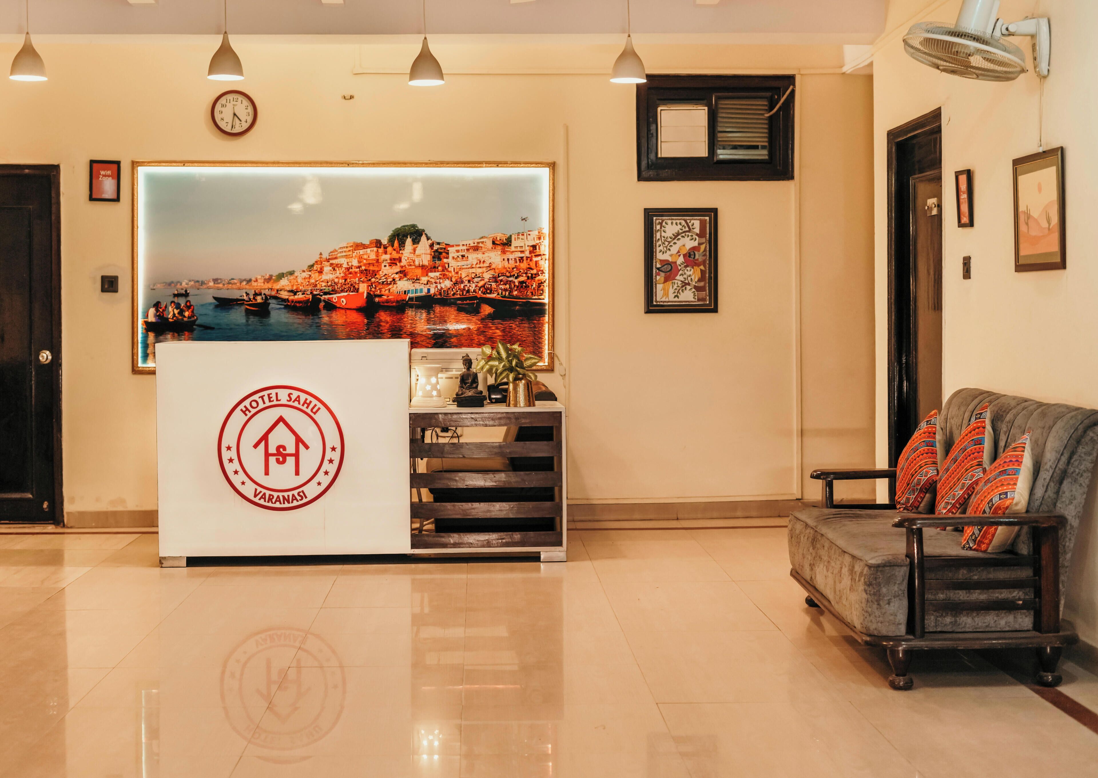 A hotel reception desk with a cityscape backdrop, a clock, and a sofa with patterned cushions.
