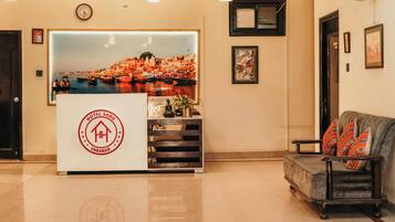 A hotel reception desk with a cityscape backdrop, a clock, and a sofa with patterned cushions.