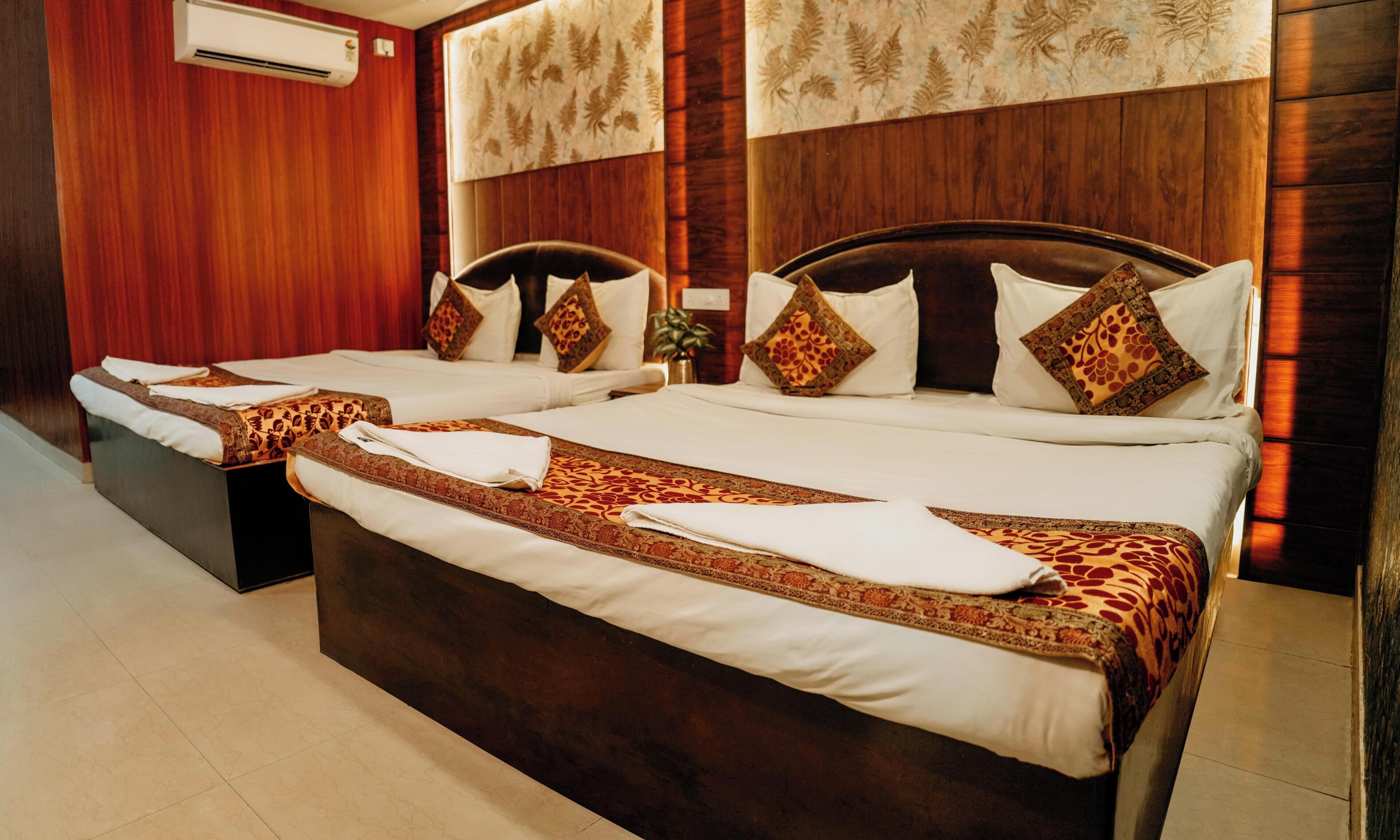 A hotel room with two beds, wooden headboards, patterned wall decor, and a tiled floor.