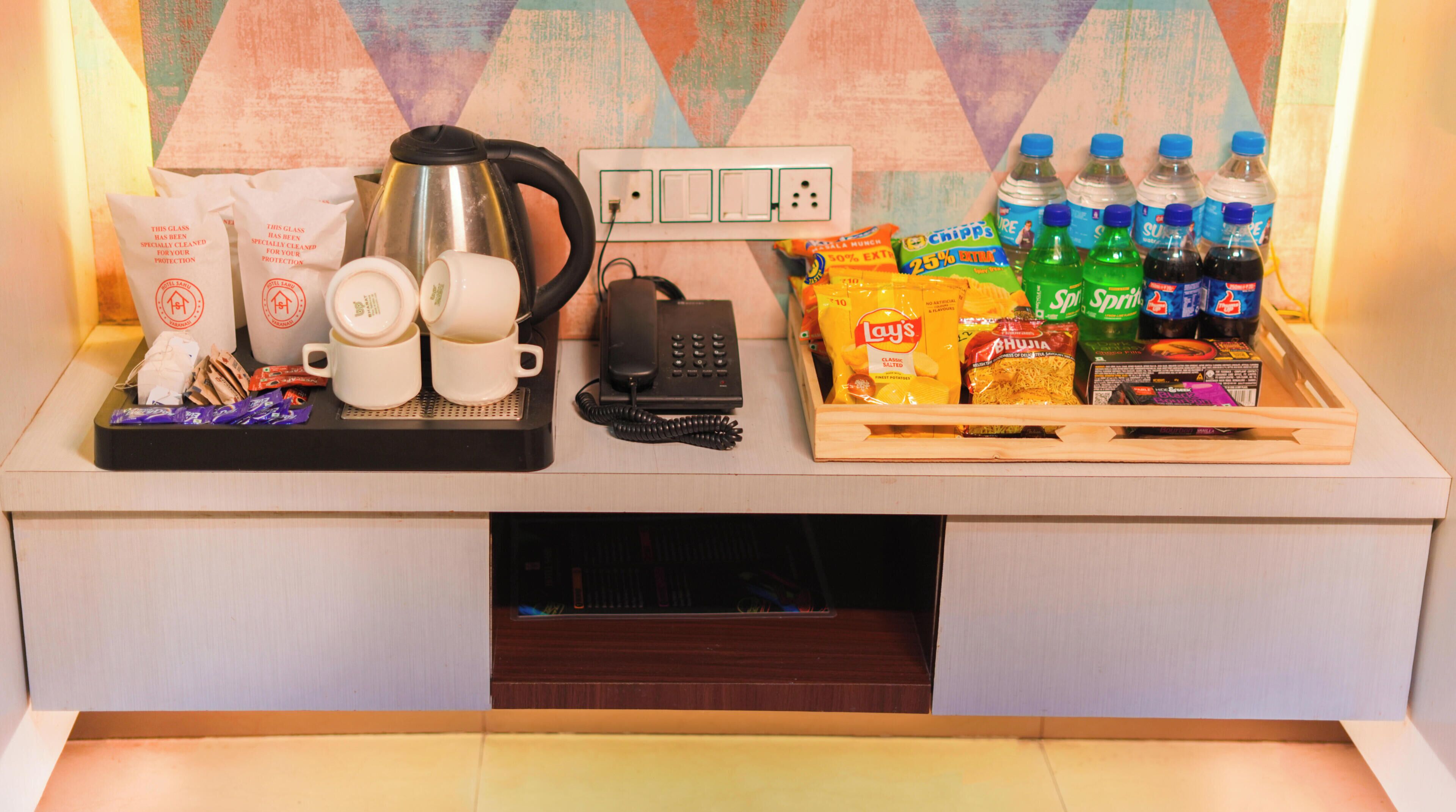 A kitchenette with a kettle, coffee maker, phone, snacks, and bottled water.