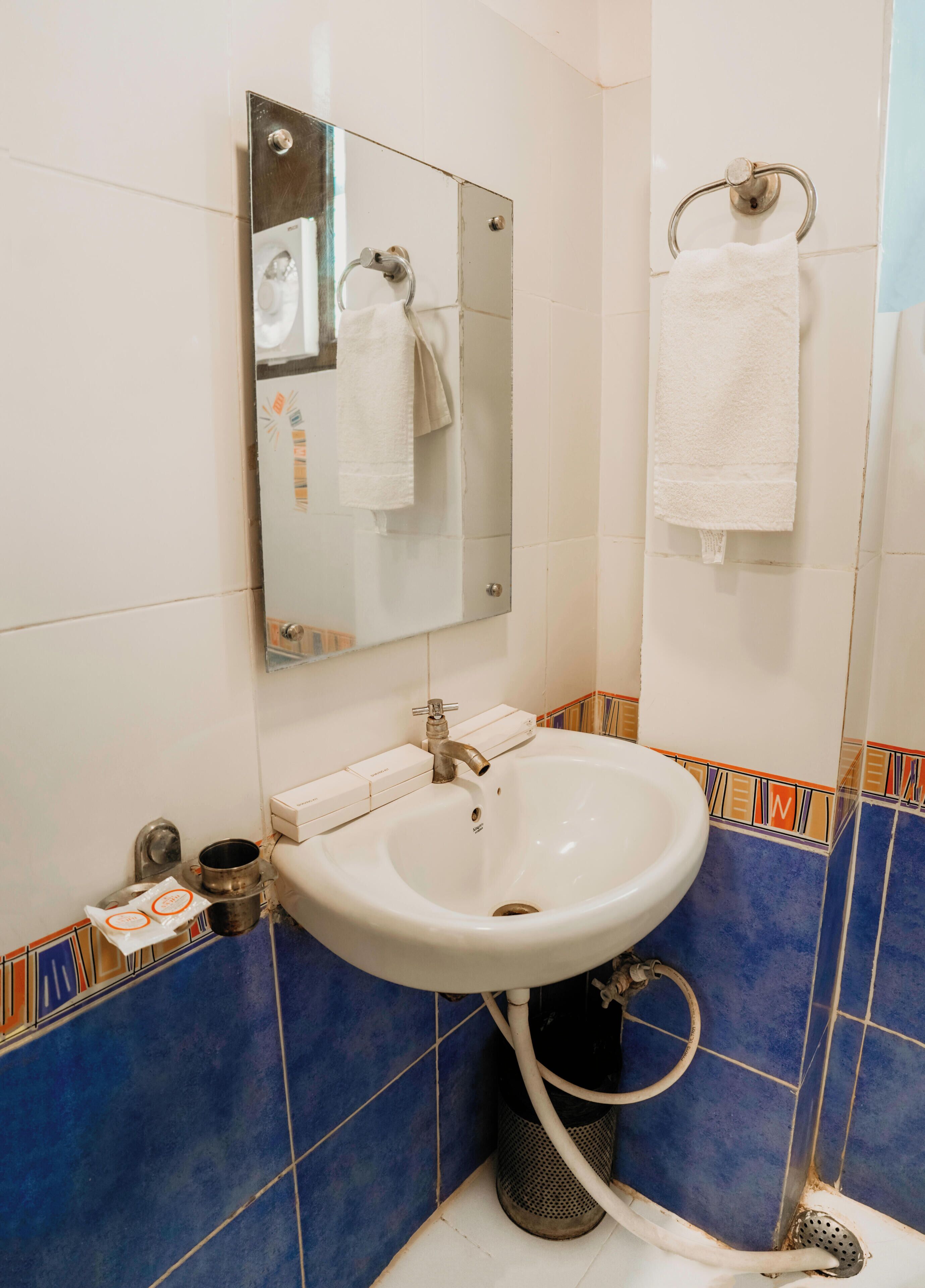 A bathroom with a sink, mirror, towel rack, and blue-tiled walls.