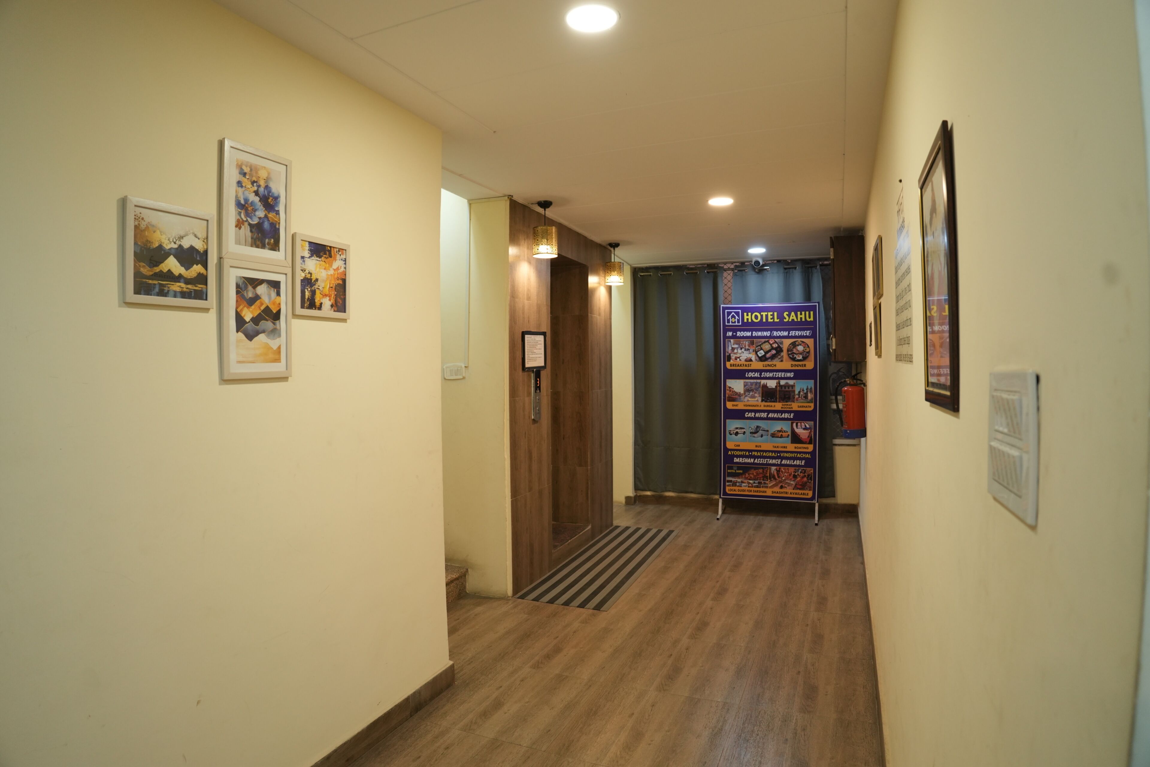 Ein Hotelgang mit gerahmten Kunstwerken an den Wänden, Holzboden und einem Empfangsbereich mit einem Schild.