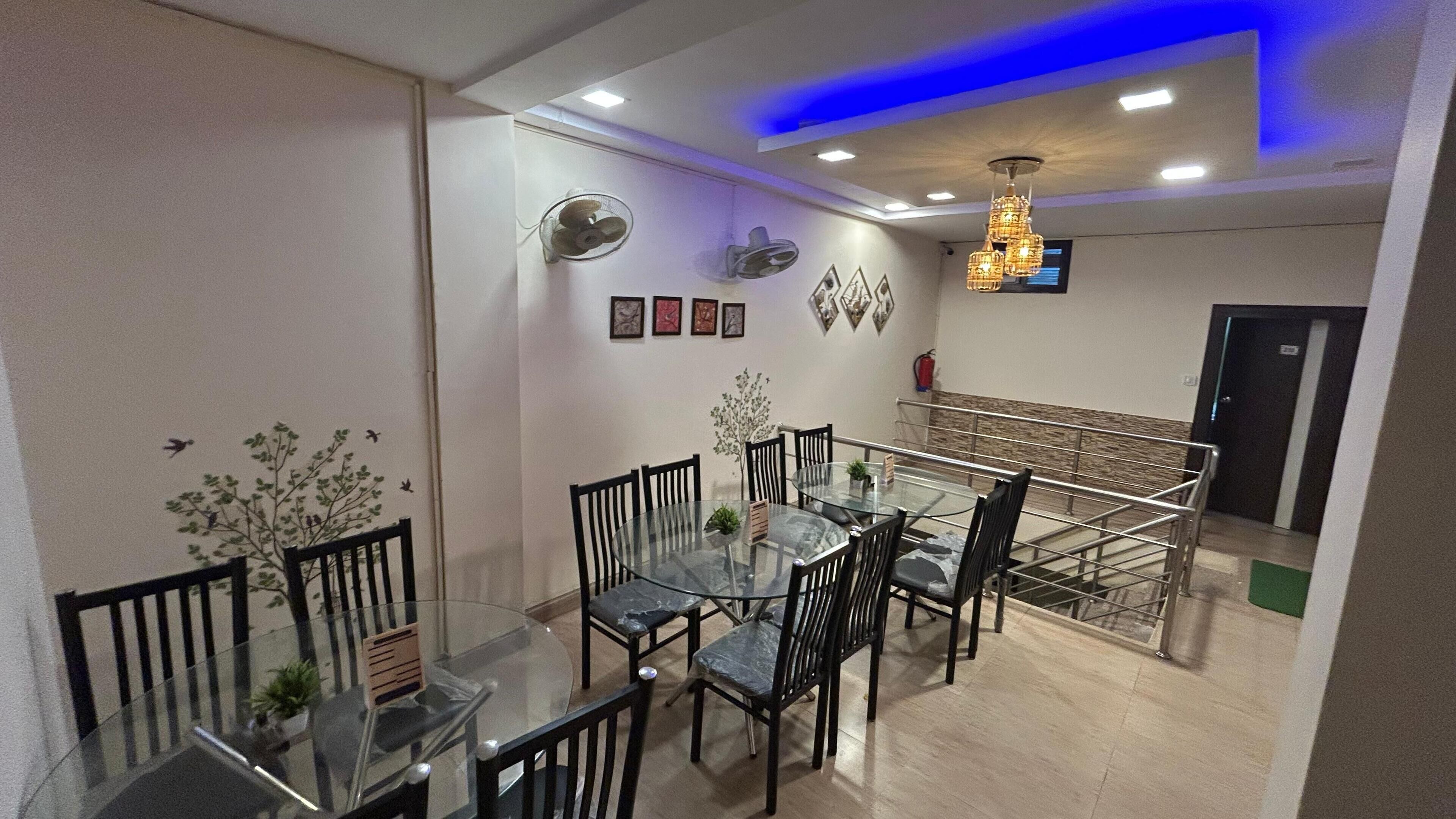 A dining area with a glass table and chairs, a ceiling fan, wall-mounted lights, and framed artwork.