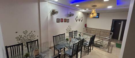 A dining area with a glass table and chairs, a ceiling fan, wall-mounted lights, and framed artwork.