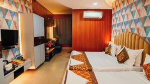 A hotel room with a TV, a desk with a lamp, a bed with patterned bedding, and a wall-mounted air conditioner. - Hotel Sahu Near Kashi Vishwanath Temple Gate (Varanasi)