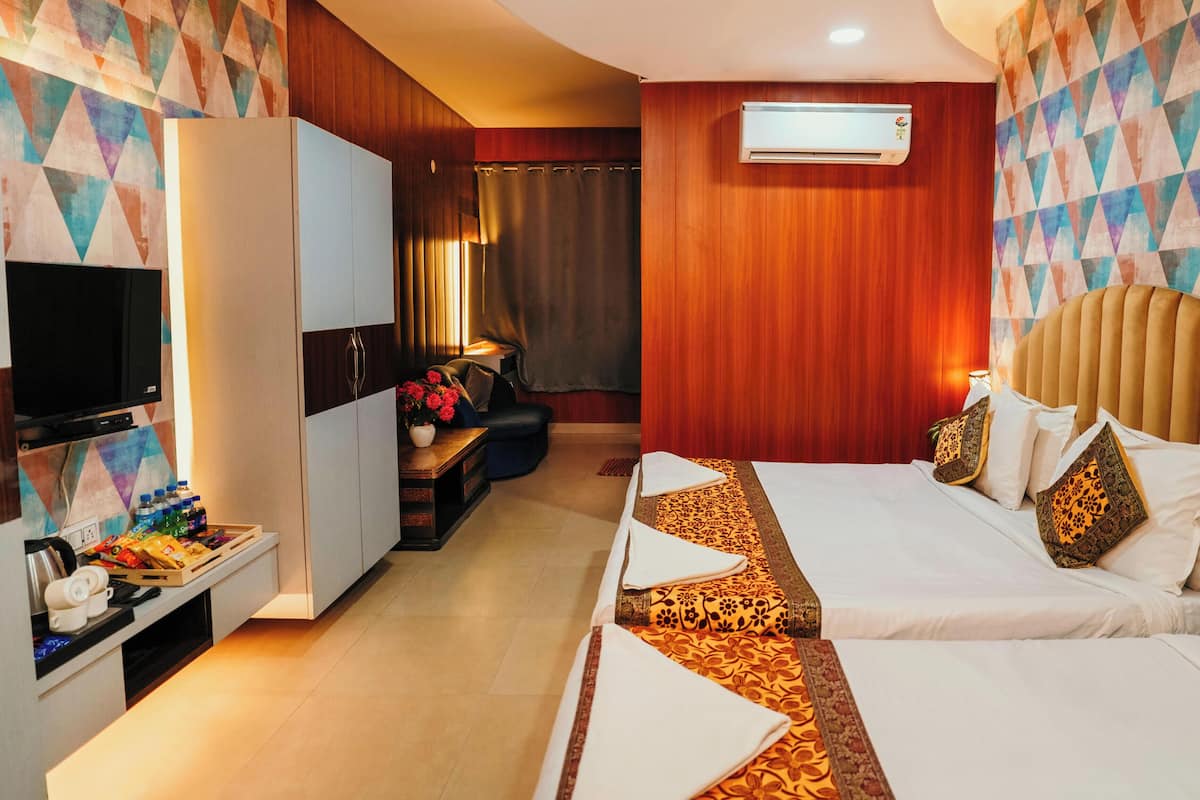 A hotel room with a TV, a desk with a lamp, a bed with patterned bedding, and a wall-mounted air conditioner.