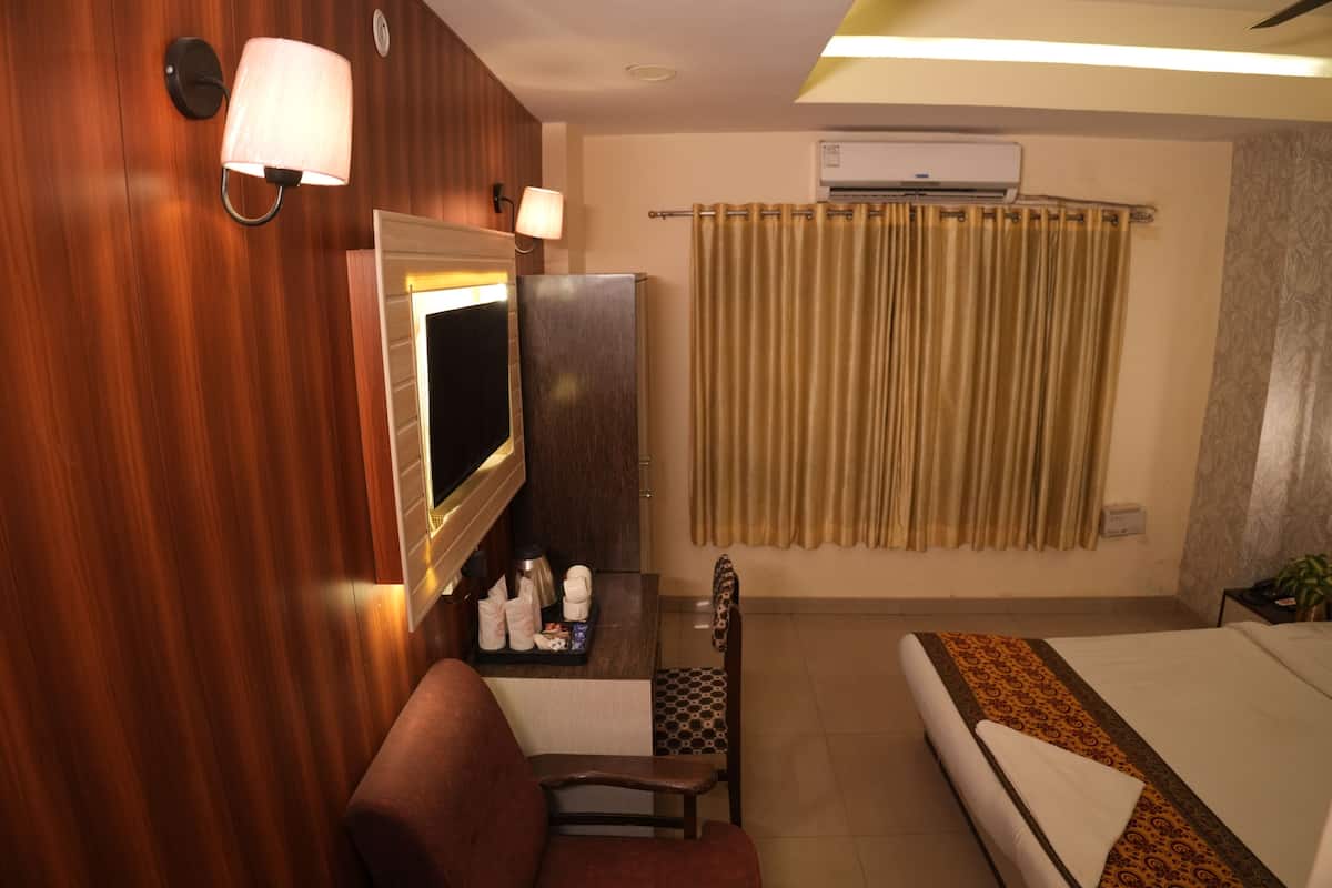 A hotel room with a wooden wall, a TV, a desk with toiletries, a bed with a patterned bedspread, and a curtain.