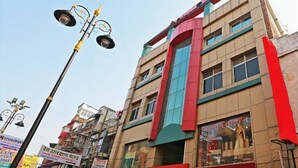 A multi-story building with a prominent red and blue facade, large windows, and a visible signboard. - Hotel Sahu Near Kashi Vishwanath Temple Gate (Varanasi)
