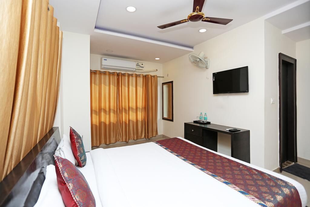 A hotel room with a bed, a desk, a television, and an air conditioning unit.