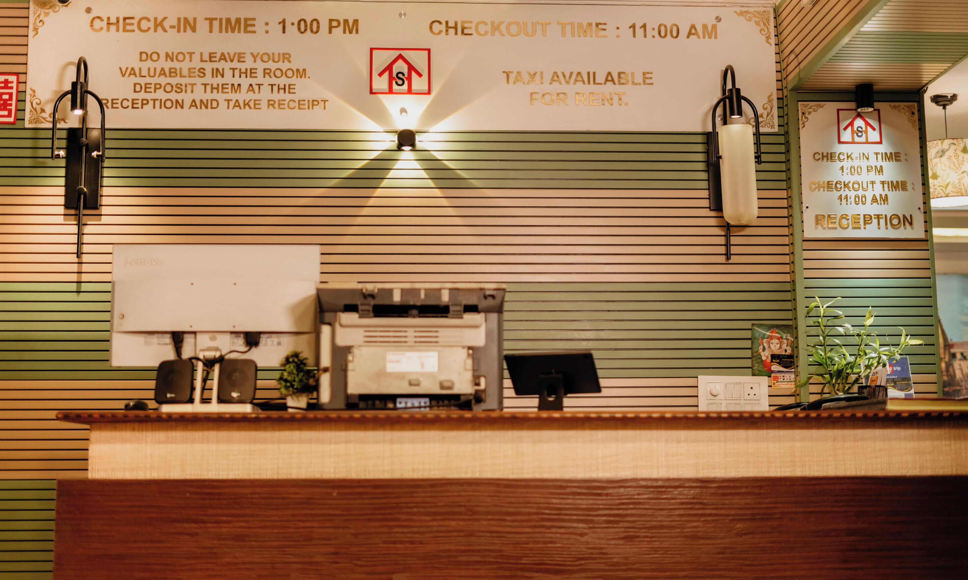 A reception desk with a sign indicating check-in and checkout times, a taxi service notice, and a security deposit instruction.