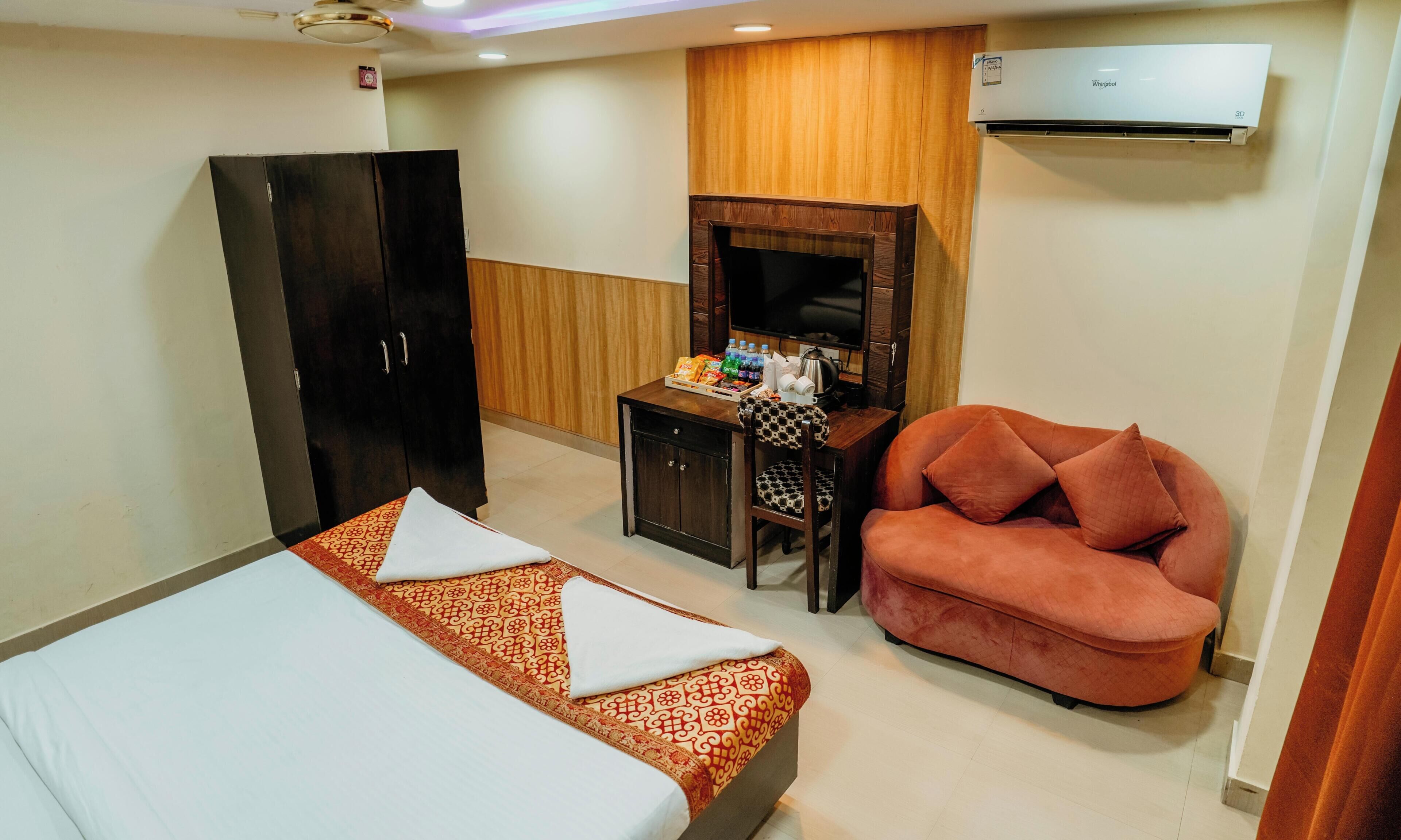 A hotel room with a bed, a sofa, a desk with a TV, and an air conditioner.