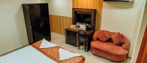 A hotel room with a bed, a sofa, a desk with a TV, and an air conditioner.