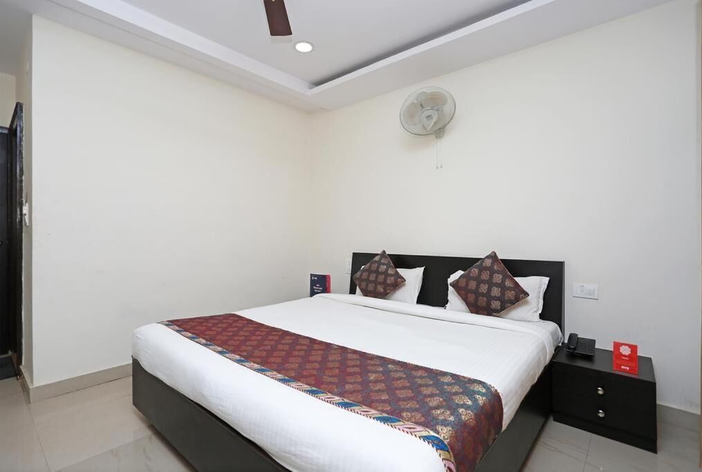 Een hotelkamer met een bed, een nachtkastje met een telefoon, een ventilator aan de muur en een deur.