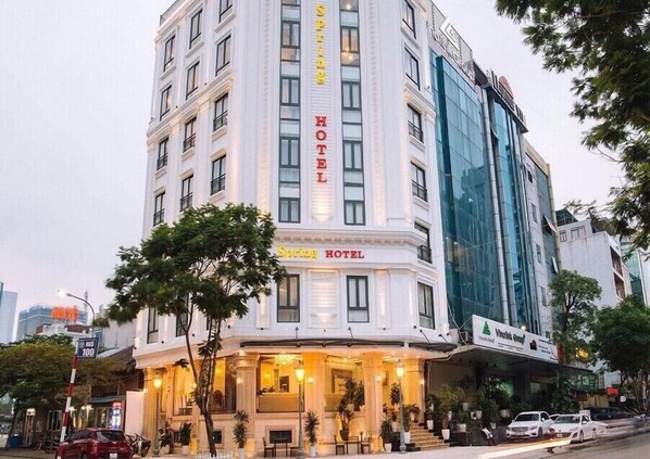 A hotel with a classic facade, a prominent sign reading "Spring Hotel," and a modern glass building adjacent to it.