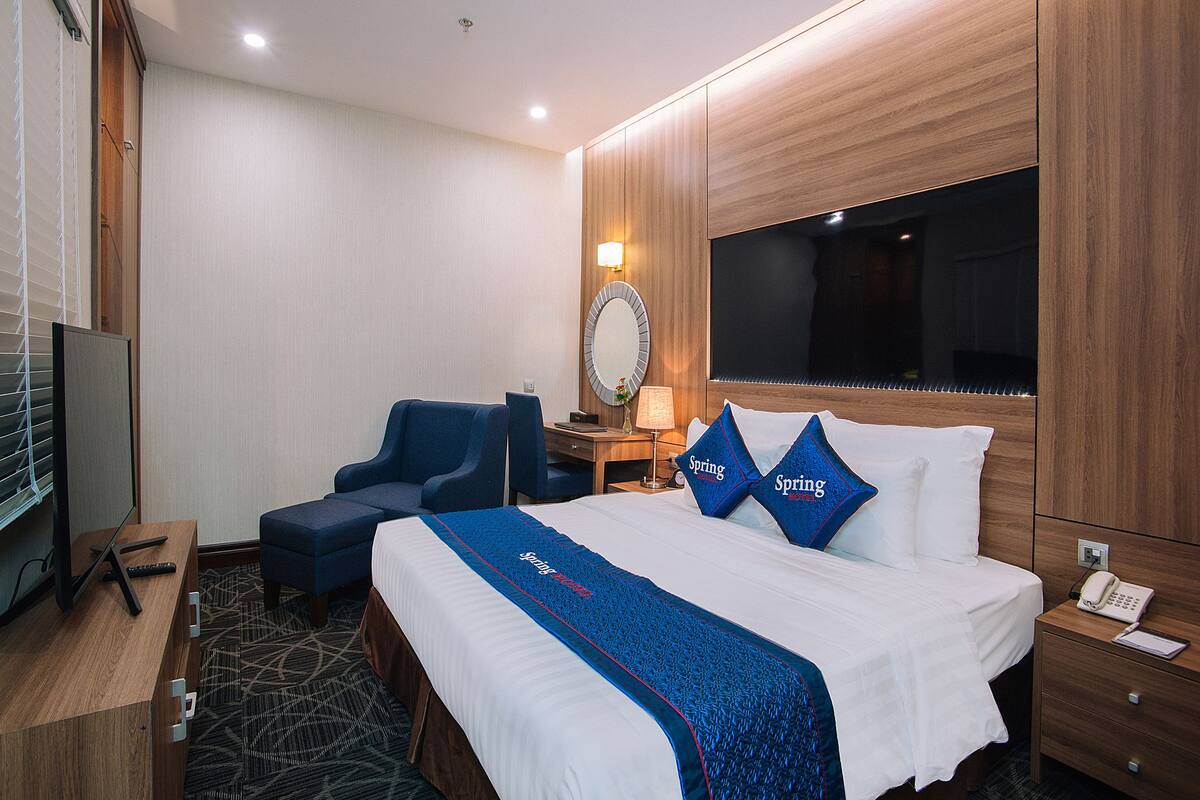 A hotel room with a large bed, a desk, a chair, a TV, and a mirror.