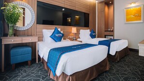 Une chambre d’hôtel avec deux lits, un bureau, une chaise, un miroir, une lampe, une plante et un tableau au mur.