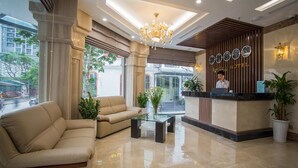 Un espace d’accueil d’hôtel au design moderne, comprenant un comptoir d’accueil, un lustre et un coin salon avec un canapé et une table basse.