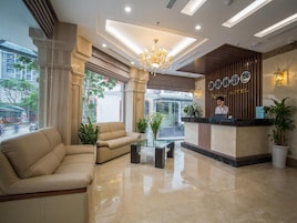 Zona de recepción de hotel con diseño moderno, que incluye un mostrador de recepción, un candelabro y un área de estar con un sofá y una mesa de centro.