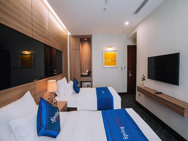 Habitación de hotel con dos camas, televisión, minibar y baño visible a través de una puerta abierta.