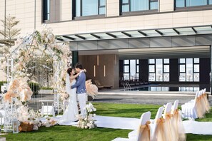 A modern building with a glass facade, a wedding ceremony setup with floral decorations, and a white aisle. - Holiday Inn Foshan Shunde (Foshan)