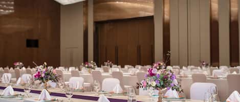 A banquet hall with tables set for events, featuring floral centerpieces and a modern chandelier.
