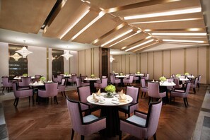 Un'ampia sala da pranzo con diversi tavoli rotondi, sedie e lampade moderne.